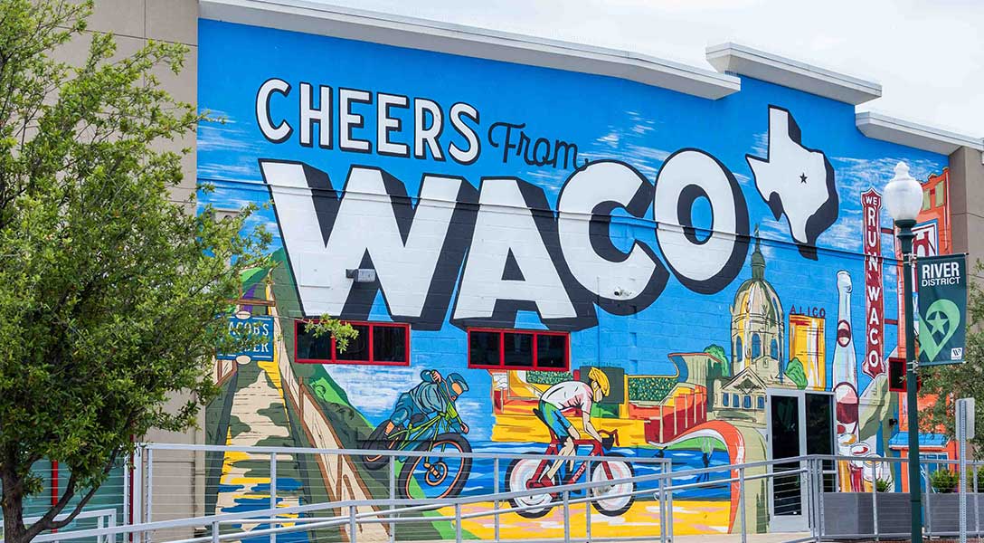 Mural of cyclists on a winding path. Text reads ‘Cheers from Waco’.