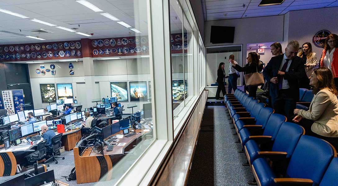 President Logan and members of her team watch the action in mission control during their visit to NASA.